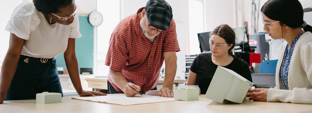 Three Industrial Design students and a professor working on a design project in a studio.