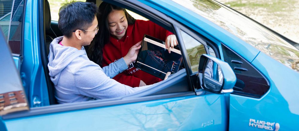 Two students work on autonomous vehicle technology inside a hybrid car.