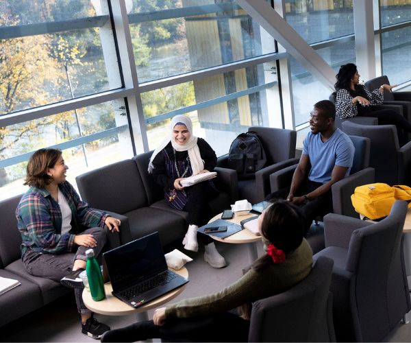 Students working together in a lounge space in front of windows.