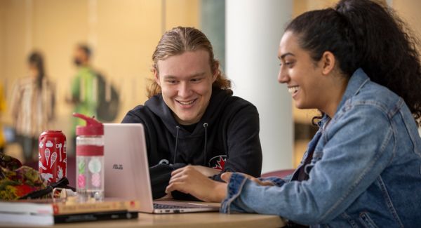 Two students working together at a table using a laptop.