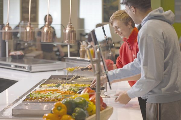 Two students getting food from a station in the Teraanga Commons Dining Hall.