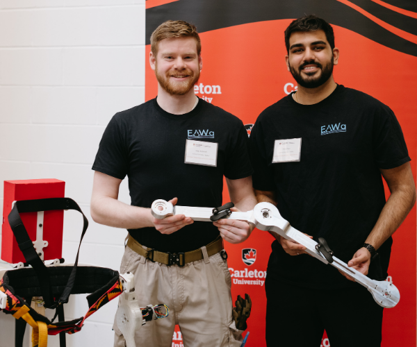 two students standing side by-side holding a mechanical tool they have created.