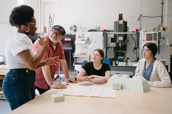 Three Industrial Design students and a professor working on a design project in a studio.